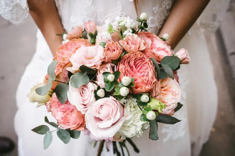 Brautstrauß aus rosa Rosen und Eukalyptus in den Händen der Braut