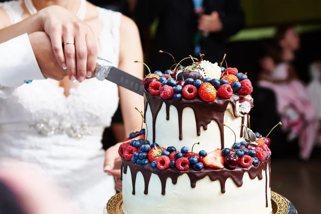 Brautpaar schneidet zweistöckige Hochzeitstorte mit Schokoladenglasur und frischen Beeren an