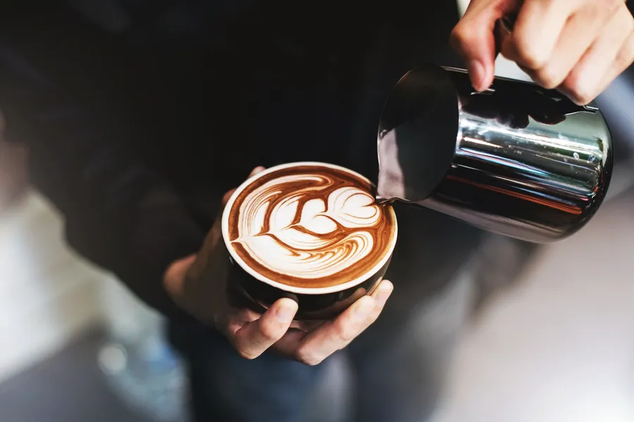 Barista gießt Milch für Latte Art in eine Kaffeetasse