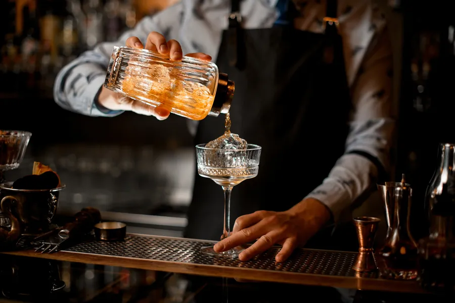 Barkeeper gießt einen Cocktail über Eis in ein Glas