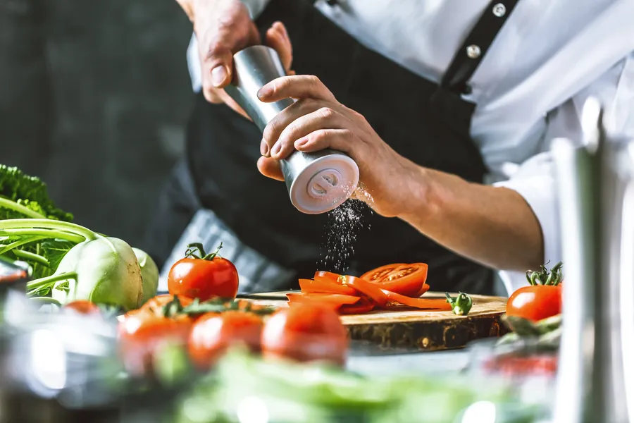 Kulinarische Erlebnisse — Chef würzt frisches Gemüse auf einem Holzbrett