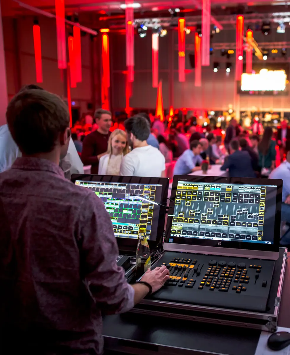 Techniker am Mischpult vor rot beleuchtetem Event